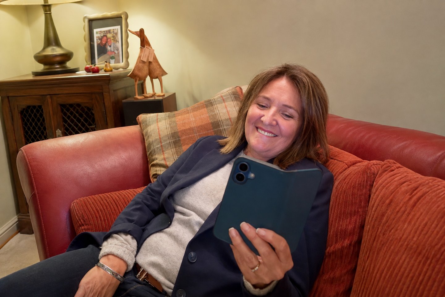 A woman on the sofa smiling at her phone while her song for a 60th birthday plays.