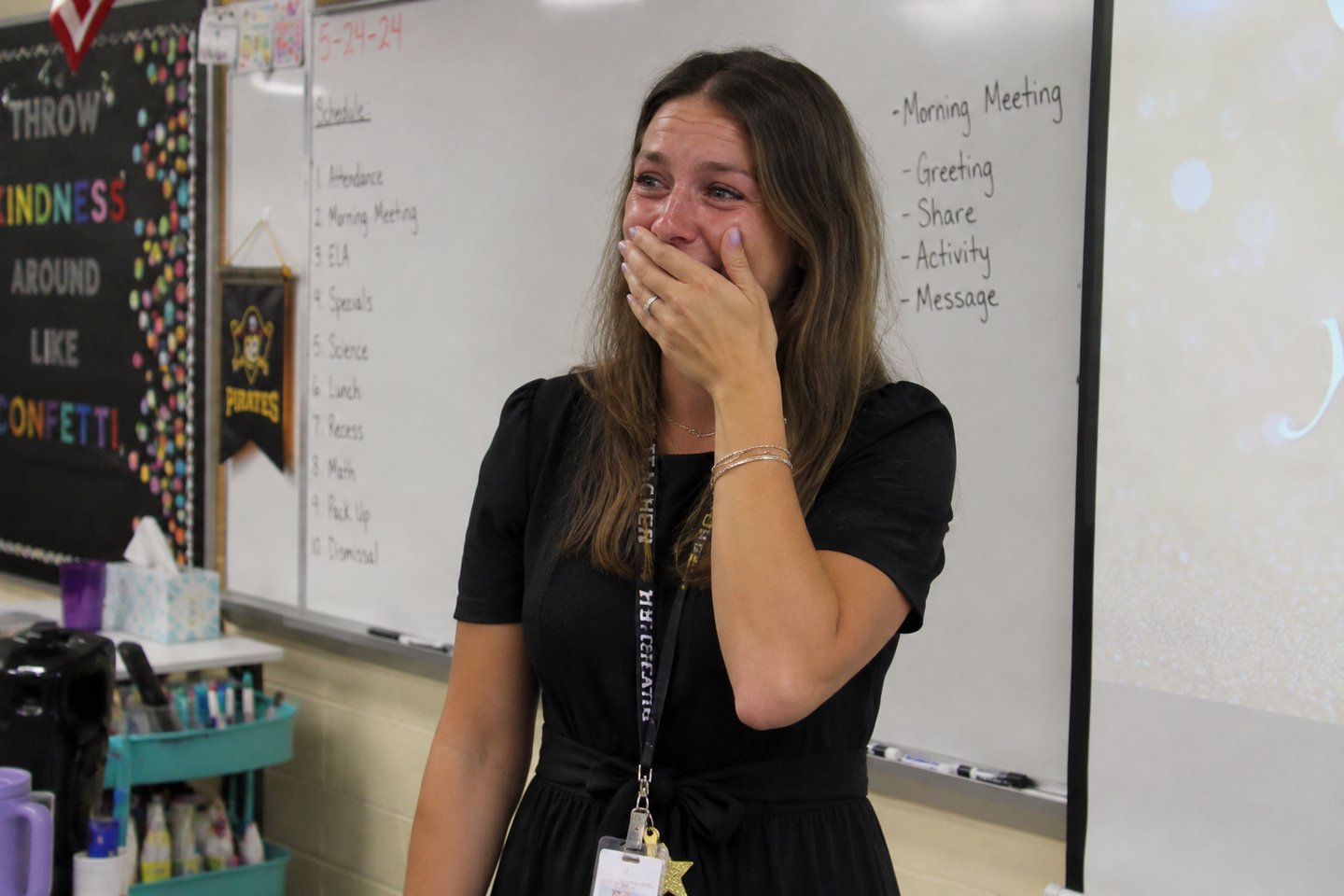 A teacher covering her mouth, moved by a song for a teacher from her students.
